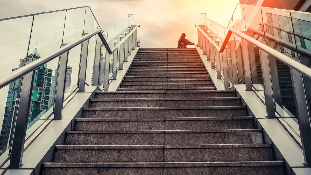 Urbane Treppe führt im warmen Gegenlicht hinauf zu Wolkenkratzern, Sinnbild für den Aufstieg aus eigener Kraft ohne Startkapital
