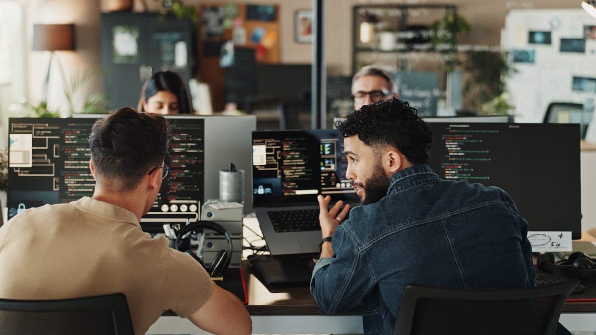 Zwei Entwickler besprechen am Abend Code vor mehreren Monitoren, typische Szene einer nebenberuflichen Gründung nach Feierabend